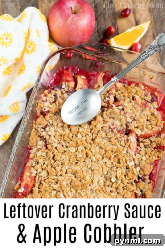 A close-up view of a baked Cranberry Apple Cobbler in a glass pan, showcasing its bubbling fruit filling and a perfectly golden-brown, textured oat crumble topping. The inviting warmth and deliciousness of the dessert are palpable.