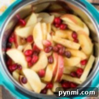 Sliced apples and cranberries simmering in an instant pot on a rustic wooden surface.