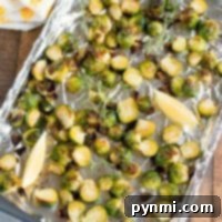 Roasted Brussels sprouts on a foil-lined baking sheet with lemon wedges, knowing just how long to bake Brussels sprouts at 450 ensures they come out perfectly caramelized.