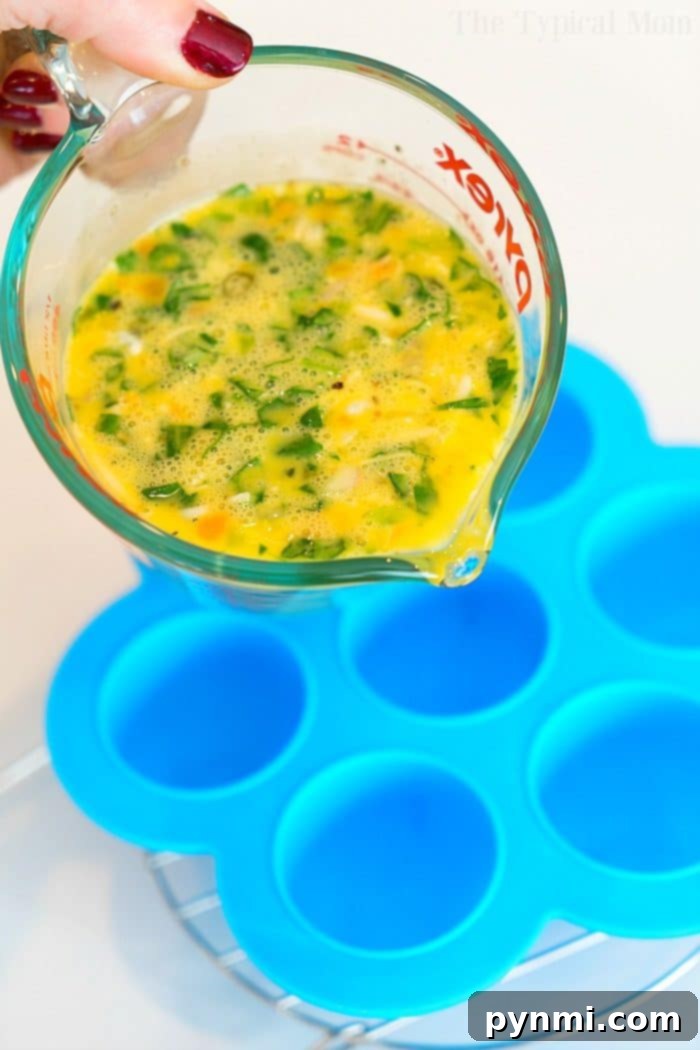 Pressure cooker egg bites are the perfect protein packed breakfast for busy mornings. A great Keto Instant Pot recipe with just a few ingredients. #instantpot #eggbites #starbucks #keto #instantpotrecipes #pressurecooker #crockpotexpress #thetypicalmom A hand pouring egg mixture with chopped vegetables from a measuring cup into a blue silicone mold on a metal rack to make pressure cooker egg bites