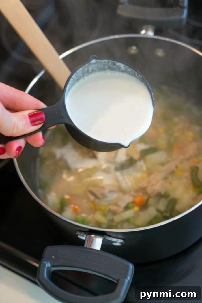 A serving of turkey pot pie soup topped with a flaky biscuit, showcasing the creamy texture and hearty ingredients.