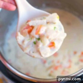 A ladle of creamy turkey pot pie soup brimming with vegetables hovers over a steaming pot.