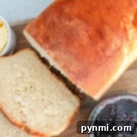 Freshly baked bread loaf with slices, alongside butter and a jar of berry jam on a wooden board, captures the cozy essence of baking bread at home.