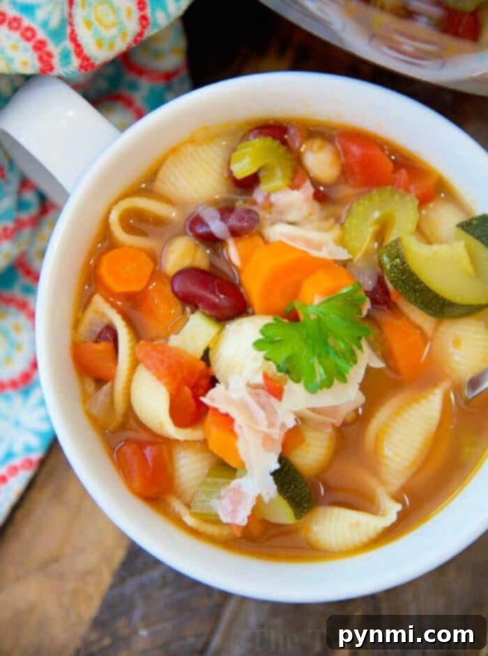 Quick Pressure Cooker Garden Soup 2 A vibrant bowl of pressure cooker vegetable soup, featuring shell pasta, robust kidney beans, fresh zucchini, crisp carrots, tender celery, and diced tomatoes, all garnished with bright parsley and a slice of savory bacon. The background showcases a warm, colorful fabric.