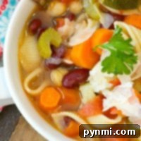 Close-up of a bowl of easy minestrone soup with pasta, carrots, zucchini, beans, and a parsley garnish, all perfectly cooked in an instant pot.