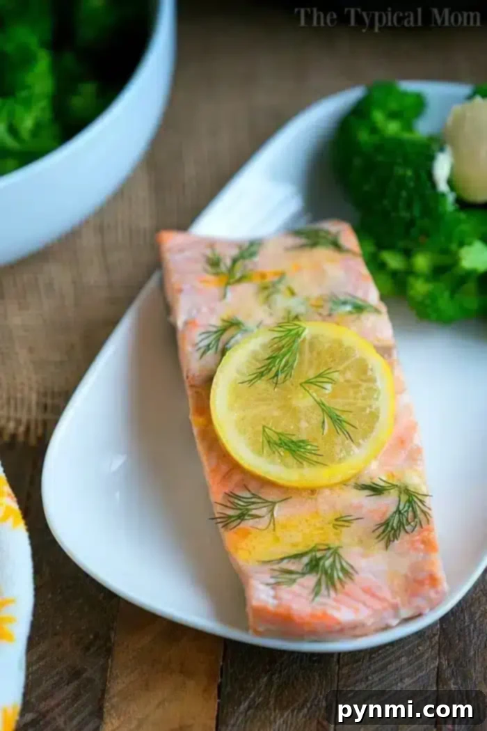 A perfectly cooked salmon fillet, garnished with a lemon slice and dill, alongside steamed broccoli, ready to serve.