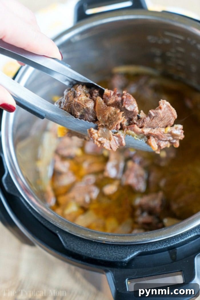 French onion pressure cooker roast is tender with tons of flavor. Perfect Instant Pot shredded beef tacos for dinner even your kids will rave about. #instantpotrecipes #instantpot #roast #frenchonion #tacos #shreddedbeef #ninjafoodirecipes #crockpotexpressrecipes #pressurecookerrecipes Close-up of a French onion beef being served with tongs from a pressure cooker, highlighting its tender texture.