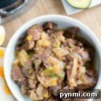 Effortless French Onion Pressure Cooker Roast 4 A bowl of shredded beef with onions, reminiscent of French onion flavors, is served beside an avocado half on a wooden surface.