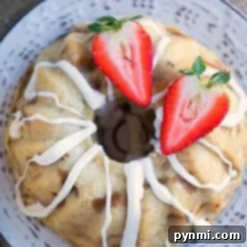 A bread pudding bundt cake with white icing, topped with halved strawberries, sits gracefully on a decorative plate, reminiscent of the cozy warmth that instant pot bread pudding brings to a home.