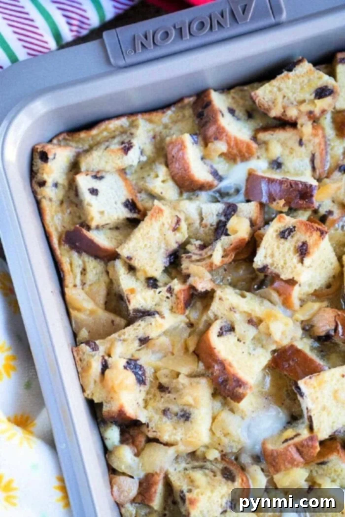 A baking pan filled with a delightful raisin bread pudding, featuring cubed bread pieces, some toasted. The mix of bread and creamy custard is studded with raisins and perhaps chocolate chips. The pan rests on a vibrant, colorful tablecloth.