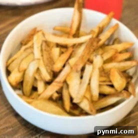A bowl of golden-brown homemade French fries, perfectly crisped using the Ninja Foodi, sits invitingly on a wooden table.