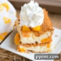 A slice of delightful peach angel food cake topped with whipped cream sits gracefully on a white square plate. The light, fluffy cake reveals juicy peach chunks. A patterned cloth accentuates the scene alongside a baking dish, creating an inviting and warm presentation.