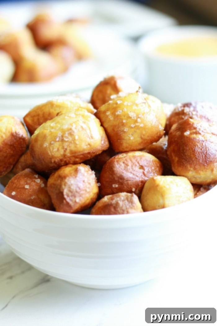 A collection of golden air fryer pretzel bites in a rustic bowl, with a mustard dip in the background.