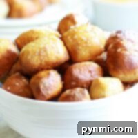 A white bowl filled with air fryer pretzel bites, perfectly salted, with a cheese dipping sauce in the background.