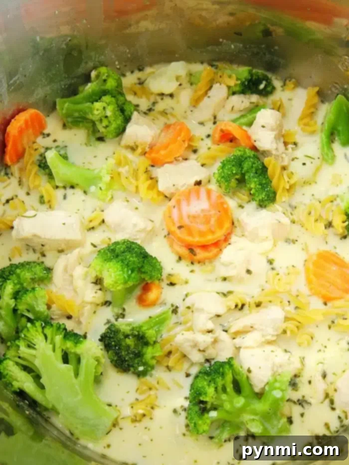 An inviting bowl of Instant Pot chicken pasta filled with spiraled noodles, bright green broccoli florets, and sliced carrots, all coated in a rich, creamy sauce and garnished with fresh herbs.
