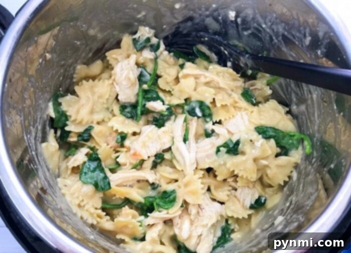 A bowl of creamy pressure cooker chicken pasta, rich with sauce, chicken, and mixed vegetables, garnished with fresh herbs.