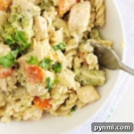 A bowl of creamy Instant Pot chicken pasta with chunks of broccoli and carrots, garnished with cilantro. A fork is placed on the edge of the bowl.