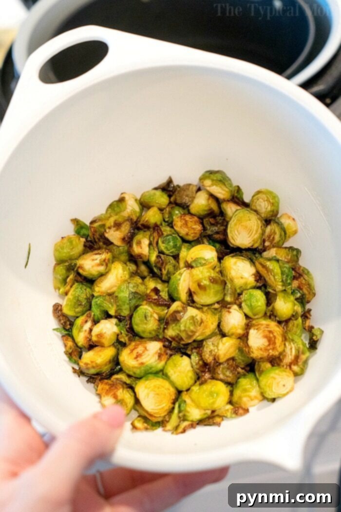 Brussel sprouts in the air fryer are just amazing! Tender brussels with a bit of a crispy outside will get you to love this understated vegetable. #brusselsprouts #brusselssprouts #airfryer #airfryerbrusselsprouts #lemon #healthy #thetypicalmom A vibrant bowl of air fryer Brussels sprouts with a rich seasoning.