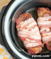 Two raw bacon-wrapped air fryer steaks sit in the basket, ready to be cooked to perfection.