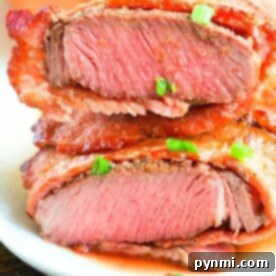 Close-up of a sliced, medium-rare air fryer steak garnished with chopped green onions on a white plate.
