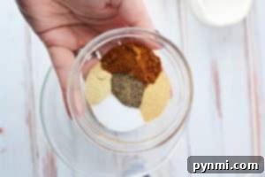 A hand holds a bowl of assorted spices and seasonings arranged in separate sections—perfect for learning how to cook steak tips in the oven with flavorful results.