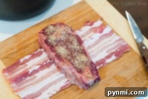 Air fryer steak, seasoned with spices, rests on bacon strips atop a wooden board with a knife nearby.