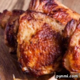 Ultimate Bone In Air Fryer Chicken Thighs 5 Roasted bone-in chicken thighs with golden-brown skin and garlic cloves sit invitingly on a wooden board, showcasing their crispy perfection achieved in the air fryer.