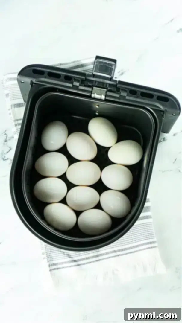 No-Boil Hard Boiled Eggs: Air Fryer Method 4 A black air fryer basket containing twelve white eggs, perfect for making air fryer hard boiled eggs, is placed on a white and gray striped cloth on a marble surface.