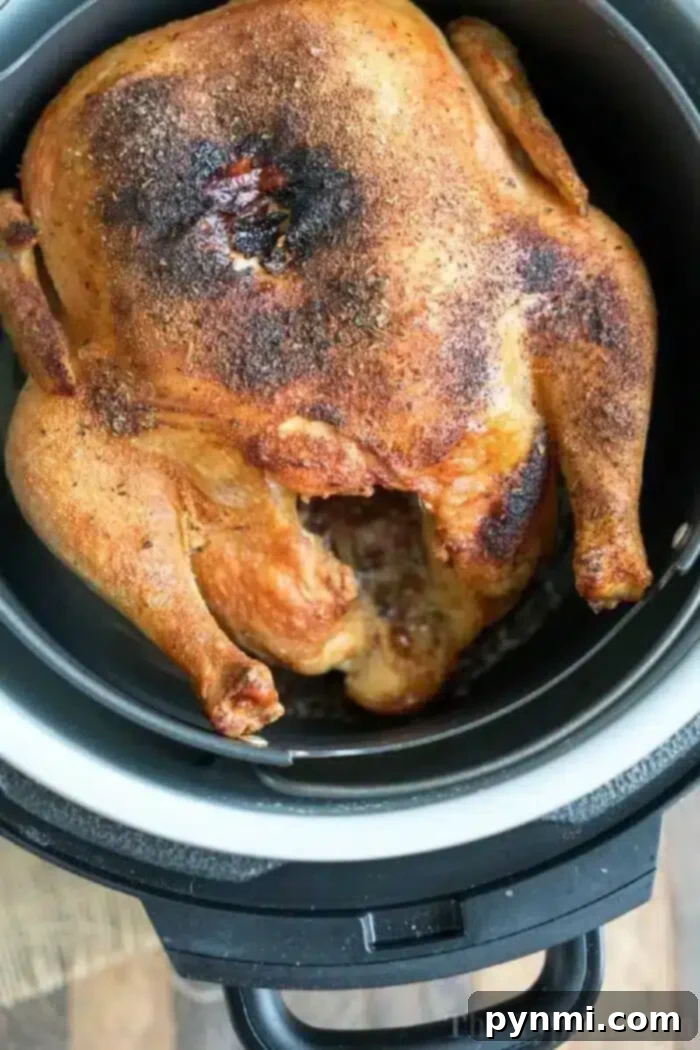 A cooked air fryer whole chicken with a seasoned, browned exterior sits in an air fryer basket. The black air fryer is placed on a wooden surface. The chicken appears to be well-roasted with crispy skin.