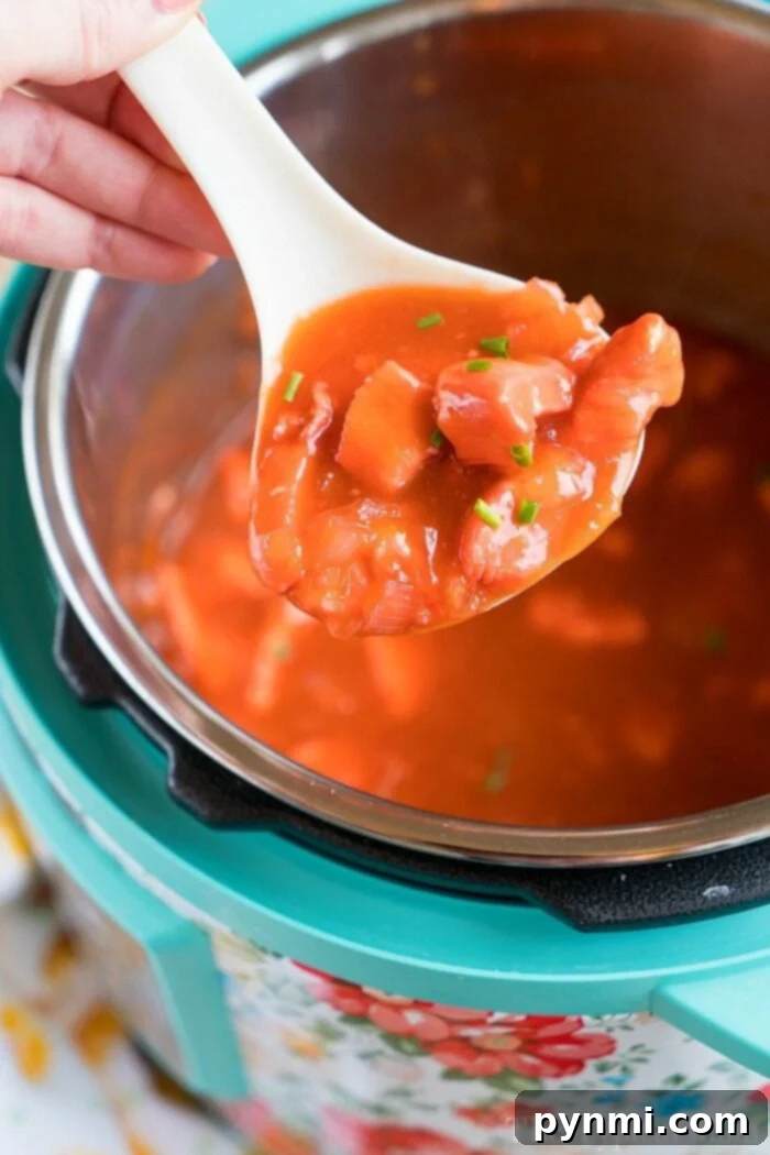 Pressure Cooker apricot chicken just needs 5 ingredients and is the perfect dinner atop a bed of rice! If you have an Instant Pot you've gotta' try this! #instantpotrecipes #instantpot #apricotchicken #chicken #dinner #pressurecooker #ninjafoodi #thetypicalmom A spoonful of apricot chicken held over a pressure cooker, ready to delight your taste buds.