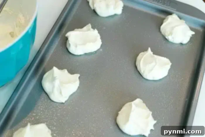 Dollops of white cream, almost as soft and airy as angel food cake, rest on a baking sheet next to a blue bowl.