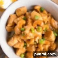 A bowl of pressure cooker cashew chicken, garnished with green onions, rests enticingly on a wooden table.