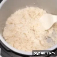 Cooked rice in a sleek Ninja Foodi rice cooker with a white plastic serving spoon inside.