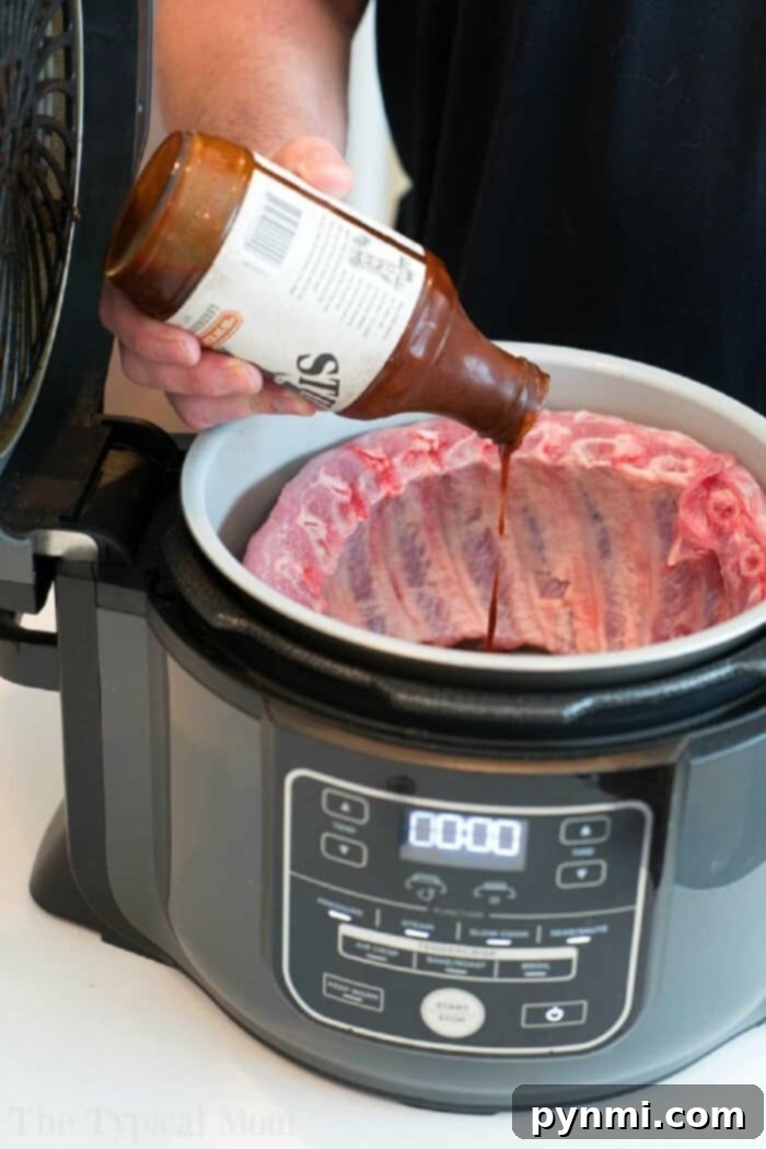 Person pouring barbecue sauce onto raw ribs in a Ninja Foodi, getting the Ninja Foodi ribs ready to be cooked to tender perfection.