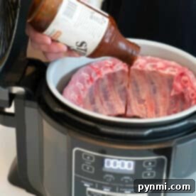 Person pouring barbecue sauce onto raw ribs in a Ninja Foodi, getting the Ninja Foodi ribs ready to be cooked to tender perfection.