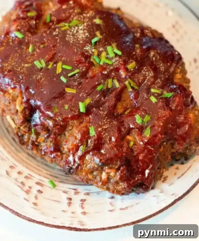 A plated portion of Ninja Foodi meatloaf topped with a glossy layer of barbecue sauce and garnished with chopped chives. The meatloaf sits on a white ceramic plate with dark streak patterns.