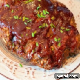Meatloaf cooked to perfection in a Ninja Foodi, topped with glaze and garnished with chopped chives on a white plate.