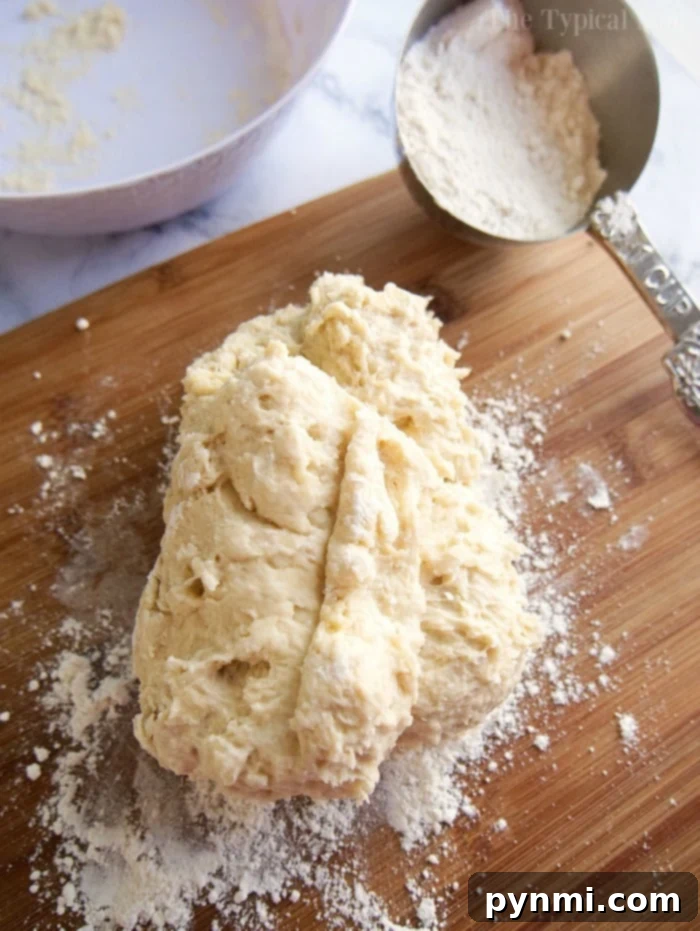 Dough on a floured wooden board with a metal measuring cup of flour nearby, ready to start your easy roll recipe.