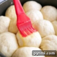 Brushing butter on raw dinner rolls in a round baking pan, this easy roll recipe promises golden perfection with minimal effort.