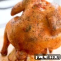 Smoked beer can chicken, perfectly roasted while standing on a can, is seasoned and cooked on a rustic wooden board.