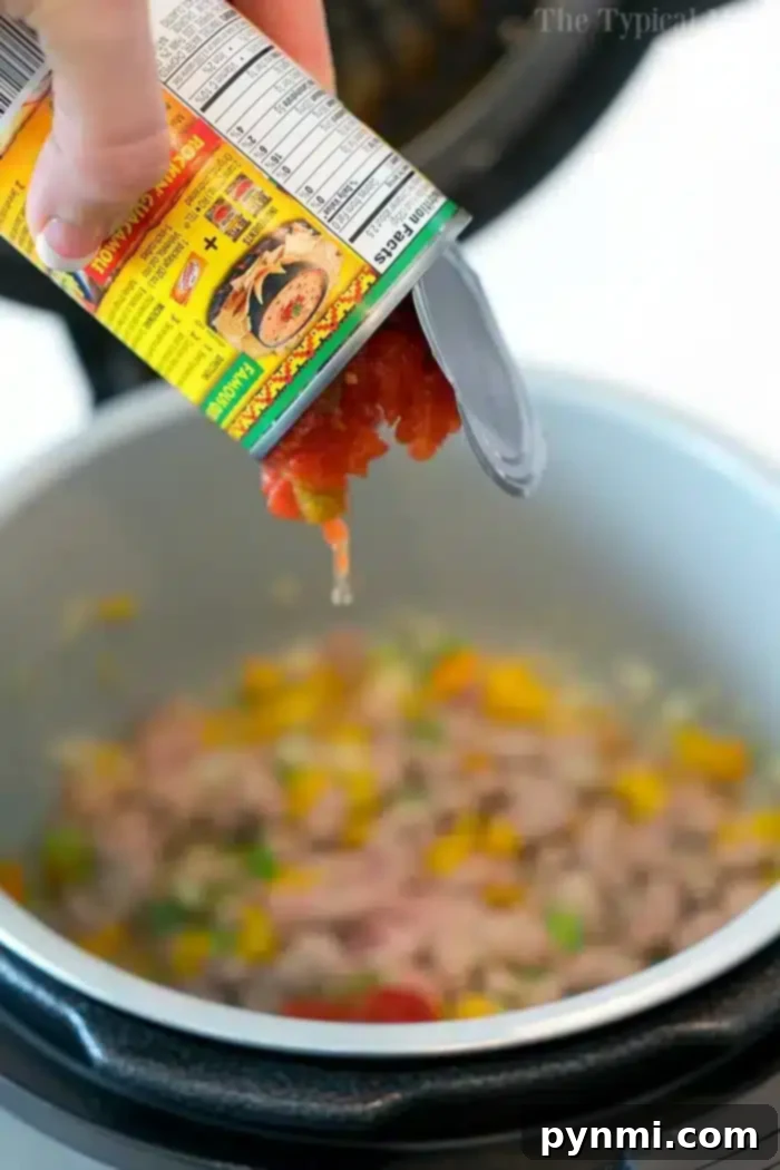 A hand pours Rotel from a can into a Crockpot Express, joining ground meat, diced yellow bell peppers, and green vegetables, ready to become a comforting Mexican casserole.
