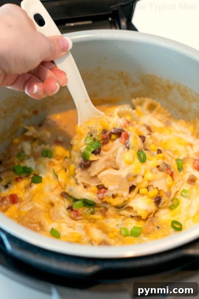 A hearty Crockpot Express Mexican casserole, packed with ground meat, corn, black beans, and pasta, is ready for serving directly from the pressure cooker, topped with melted cheese and fresh green onions.