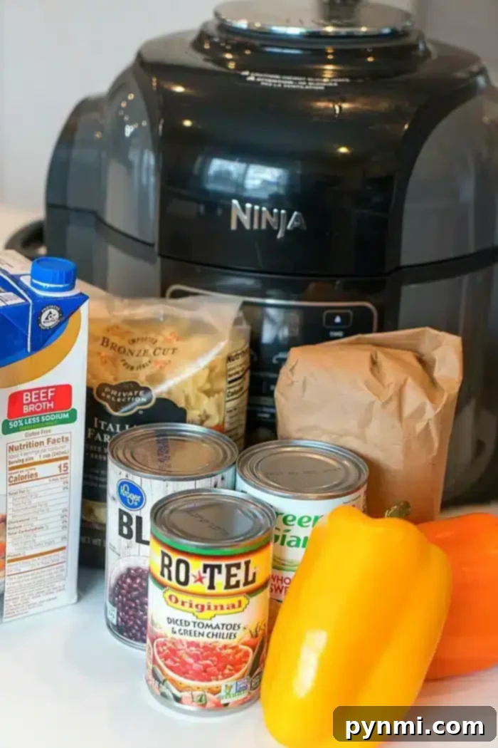 An array of ingredients, including beef broth, pasta, canned black beans, Rotel, canned peas, and a bell pepper, are neatly arranged beside a black Ninja pressure cooker, set for preparing a spicy Mexican casserole.