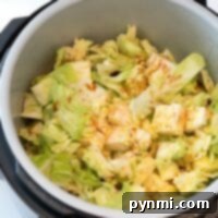 Chopped cabbage and noodles with spices simmer in a pressure cooker, sitting beside a spice container.