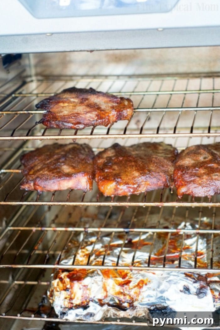 Smoked pork steaks and pork chops roast in an electric smoker, showcasing a beautiful bark and juicy interior.