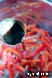 Soy sauce cascades from the measuring cup, enveloping the sliced red peppers in the pressure cooker to create a flavorful Chinese pepper steak.
