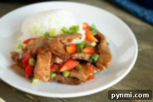 A plate of Chinese pepper steak, cooked to perfection in a pressure cooker, features tender beef stir-fry with red peppers, green onions, and a serving of fluffy white rice.