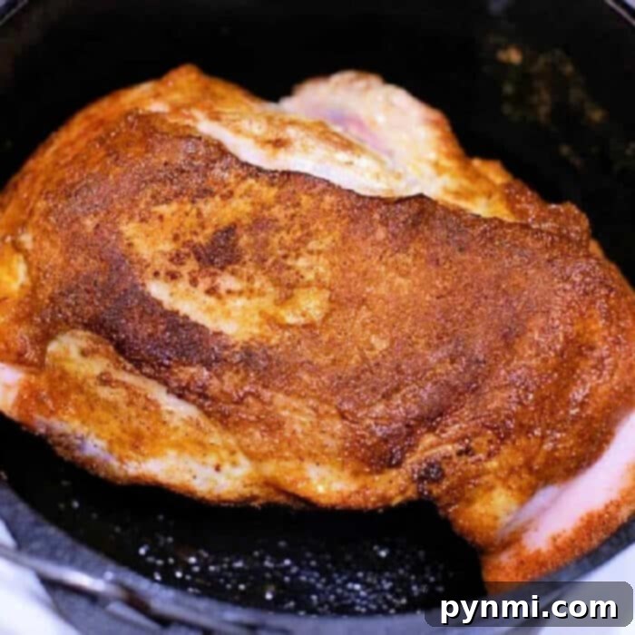 Succulent Braised Pork Roast 2 A perfectly seasoned pork roast cooking in a black cast iron skillet, showcasing a golden-brown crust. This culinary masterpiece rests confidently on the stove, reminiscent of a delicious Dutch oven dish.