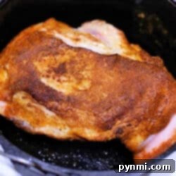 A piece of perfectly seasoned pork roast is cooking in a black cast iron skillet. The meat boasts a golden-brown crust, indicating it's being seared or roasted to perfection. While it may remind you of a good dutch oven dish, this culinary masterpiece rests confidently on the stove's cooking surface.
