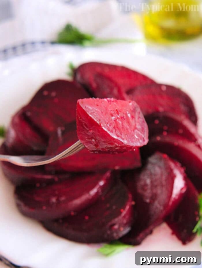 Simple Whole Instant Pot Beets 2 Close-up of a fork holding a slice of cooked beet, tenderly prepared using an Instant Pot, on a plate with more beet slices in the background.